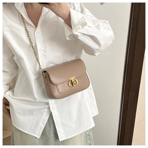 Détail du sac bandoulière beige avec fermoir doré et bandoulière chaîne sur chemise blanche