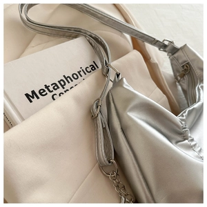 Detailed close-up of a silver pleated bow handbag with metallic sheen and chain strap