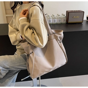 Minimalist beige tote bag with side drawstring details worn by a model in a cozy setting