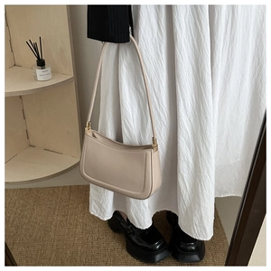 Detailed view of beige faux leather handbag with gold hardware on a minimalist background