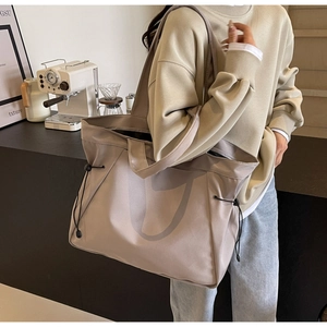 Detail view of a large beige tote bag featuring a drawstring side and nylon fabric