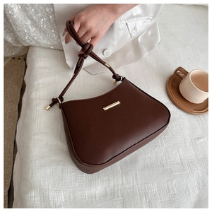 Détail du sac à bandoulière marron avec poignée tressée et barre dorée sur tissu blanc
