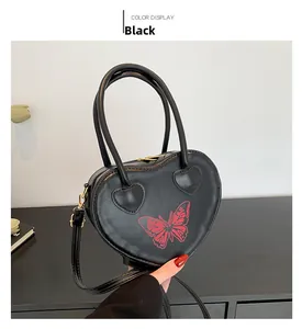 Detail of black heart-shaped handbag featuring a red butterfly print and gold hardware