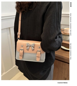 Detail of elegant contrast color messenger bag with silver bow buckle on model
