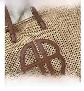 Detailed close-up of handmade straw woven tote with brown leather circular logo patch