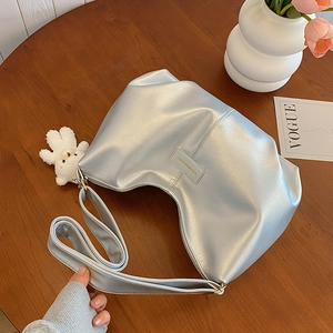 Silver soft leather tote bag with plush bear charm and metallic finish on wooden table
