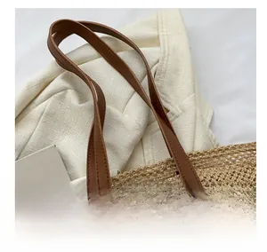 Close-up of woven straw tote bag featuring reinforced brown leather handles and mesh texture