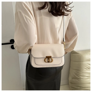 Détail d'un sac à bandoulière blanc crème avec liseré noir et fermoir rotatif doré