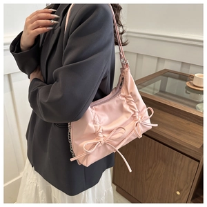 Close-up of pink satin pleated underarm bag with bow details and metal chain strap