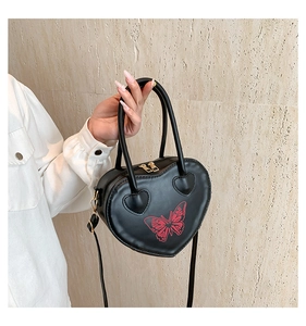 Detail of black heart-shaped handbag featuring red butterfly print and gold hardware