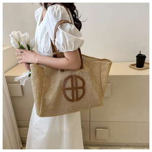Detail of large woven straw tote bag with brown leather straps and laser-cut logo decoration