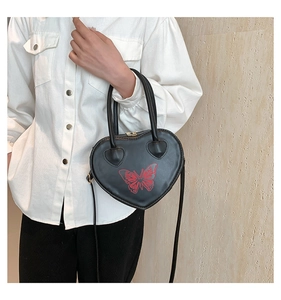 Detail of heart-shaped black bag with red butterfly print and metal zipper closure