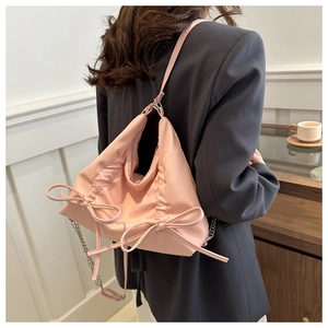 Detail of pink bow shoulder bag with pleated texture and silver chain strap on model