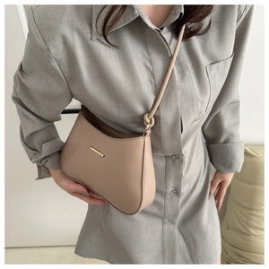 Detail of minimalist beige half-moon shoulder bag with sleek gold hardware and knotted strap