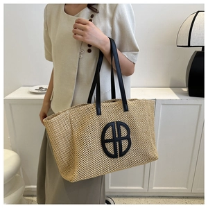Detail of woven straw tote bag with black leather HB logo and dual leather handles