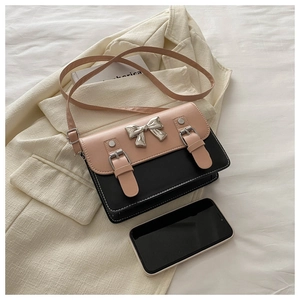 Detail of pink and black crossbody bag with metal bow buckle and phone for size scale