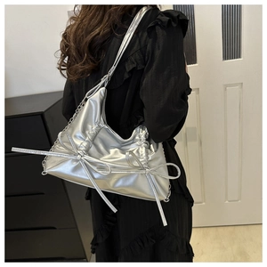Detail of silver pleated shoulder bag with bow ribbon and metallic chain on a model