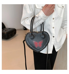 Close-up of heart-shaped black leather bag with red butterfly print and gold zipper