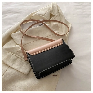 Detail of color-block PU leather bag with white contrast stitching on a beige blazer