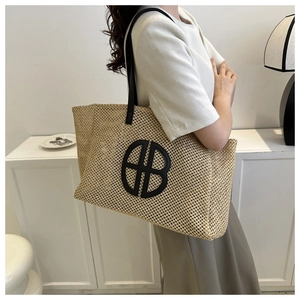 Macro shot of large woven straw tote with black leather straps and circular logo detail