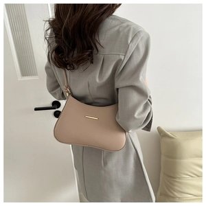 Detail of minimalist beige half-moon shoulder bag featuring gold metal bar and knot design