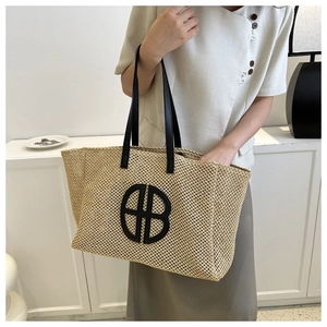 Detail of beige woven tote bag with black leather handles and circular logo