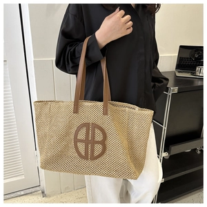 Close-up of woven straw tote bag with brown leather handles and large B logo on front