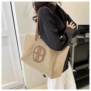 Detailed close-up of a woven straw tote bag featuring brown leather logo and long straps