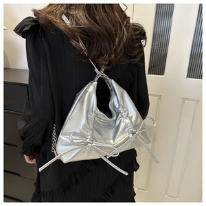 Silver metallic bow tote bag with pleated design and chain strap worn by a model