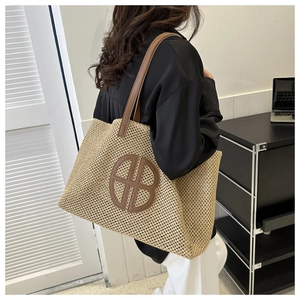 Detail of hand-woven straw tote bag featuring brown leather straps and circular logo