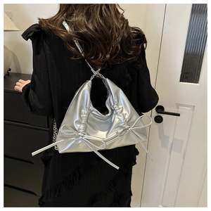 Close-up of a silver ruffled handbag with bow details worn on a black lace dress