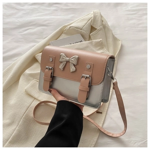 Detail of a pink and silver crossbody bag with a metallic bow and buckled leather straps