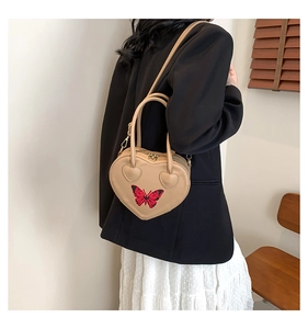 Detailed view of beige heart-shaped handbag with red butterfly embroidery and strap