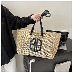 Detail of woven straw tote bag with black leather logo and shoulder straps on desk