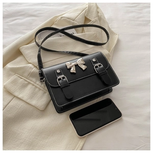 Close-up of black PU leather crossbody bag with silver bow buckle on white blazer