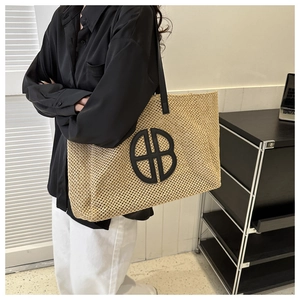 Detail of woven straw tote bag with black shoulder straps and circular logo design