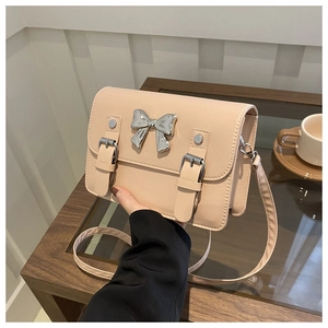 Close-up of beige crossbody bag featuring a silver metal bow and buckle straps