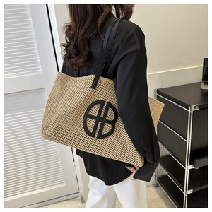 Detail of woven straw tote bag with black leather straps and large circular logo