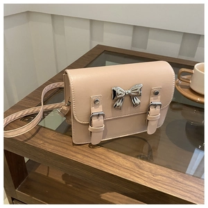 Close-up of beige satchel bag with silver metal bow and double strap magnetic closure