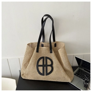 Detail view of woven straw tote bag with black leather straps and circular logo accent