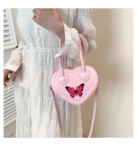Pink heart-shaped handbag with butterfly pattern detail worn by model in dress