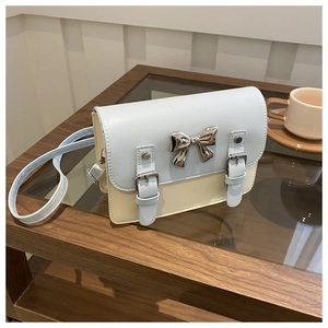 Detail of light blue and beige crossbody bag with a silver metal bow on the wooden table
