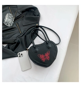 Top view of heart-shaped black handbag with red butterfly detail and accessories