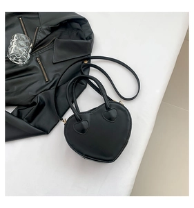 Detail view of heart-shaped black leather bag with gold hardware on a white surface