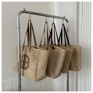Detail view of woven straw tote bags with brown and black contrast leather handles