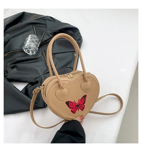 Detail of beige heart-shaped bag with red butterfly embroidery on a black leather jacket