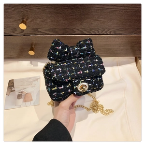 Detail of black tweed crossbody bag with bow decoration and gold chain strap