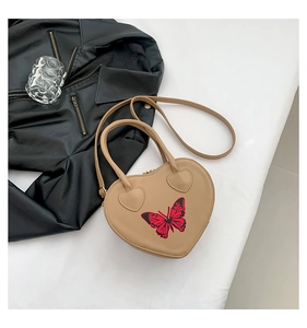 Detail view of heart-shaped beige handbag with red butterfly print and top handles