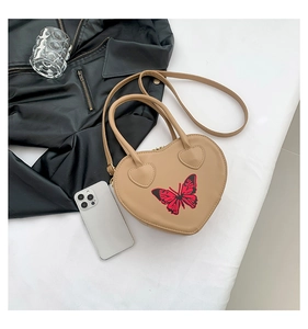 Detailed top view of a beige heart-shaped handbag with a butterfly pattern and crossbody strap
