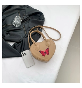 Close-up of heart-shaped beige bag featuring delicate butterfly pattern and top handle